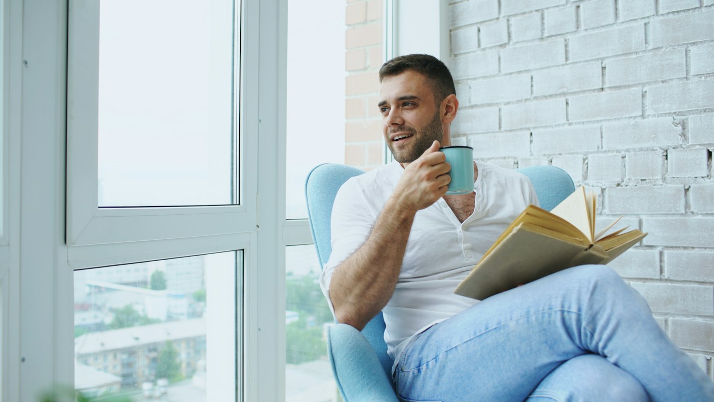 Man relaxing with a book and a cup of tea by the window
