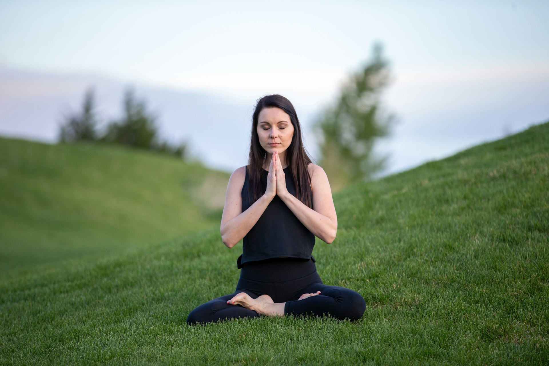 Woman meditating cross-legged on a green grassy hillside